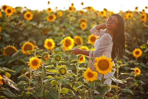 Mooie jonge zwarte vrouw draagt zomerjurk pose in een zonnebloemveld
