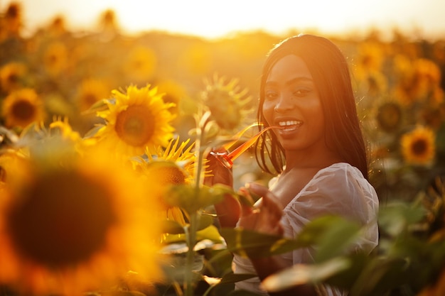 Mooie jonge zwarte vrouw draagt zomerjurk pose in een zonnebloemveld