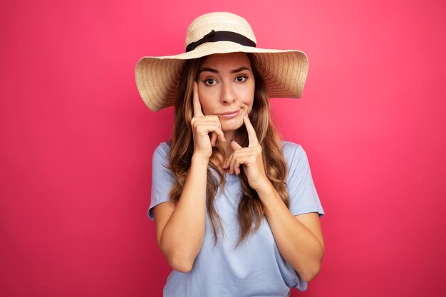 Gratis foto mooie jongedame in blauw t-shirt en zomerhoed camera kijken met sceptische uitdrukking