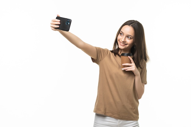 Mooie jongedame met behulp van smartphone selfie tijd, koffiekopje en mobiele telefoon geïsoleerd op wit te houden