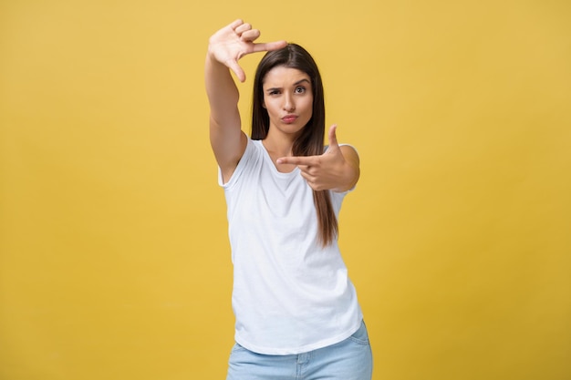 Mooie jongedame over geïsoleerde gele achtergrond glimlachend frame maken met handen en vingers met blij gezicht Creativiteit en fotografie concept