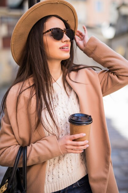 Mooie jongedame wandelen langs de straat met handtas en kopje koffie.