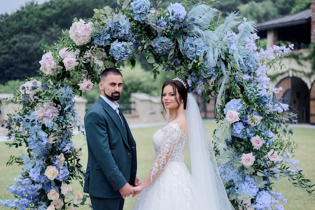 Mooie Kaukasische bruidspaar staat voor versierd met blauwe hortensia boog en hand in hand samen