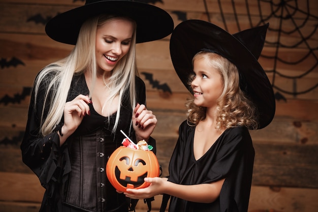 Mooie kaukasische moeder en haar dochter in heks kostuums vieren halloween met het delen van halloween snoep