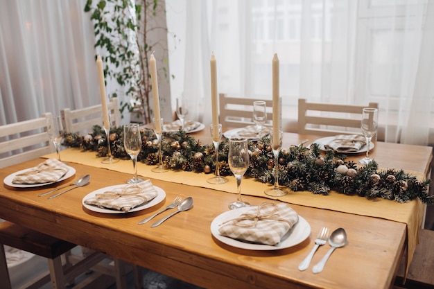 Mooie kersttafel met kaarsen en dennenboomdecoratie bij een gezellig modern interieur close-up. Vieren december vakantie nieuwjaar omringd door seizoensgebonden versierde glazen en borden