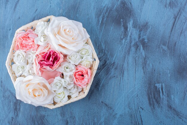 Mooie kleurrijke roze bloem in rieten mand op blauw.