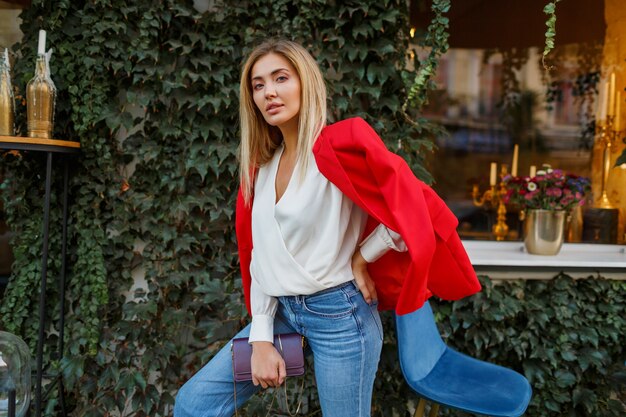 Mooie knappe blonde vrouw in rode jas poseren in stadscafé