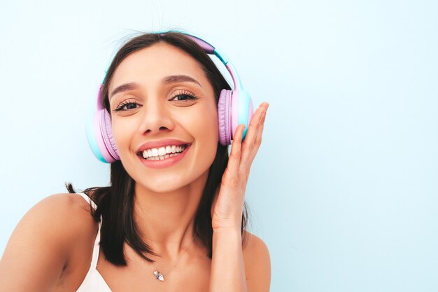 Mooie lachende vrouw gekleed in witte pyjama. zorgeloos model luistert naar muziek in draadloze koptelefoon