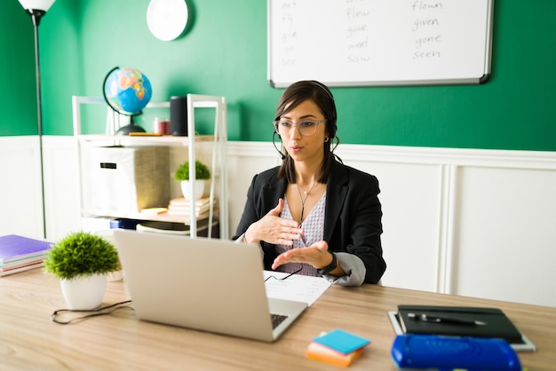 Mooie lerares met bril die met haar online leerlingen praat en een virtuele les geeft vanuit huis