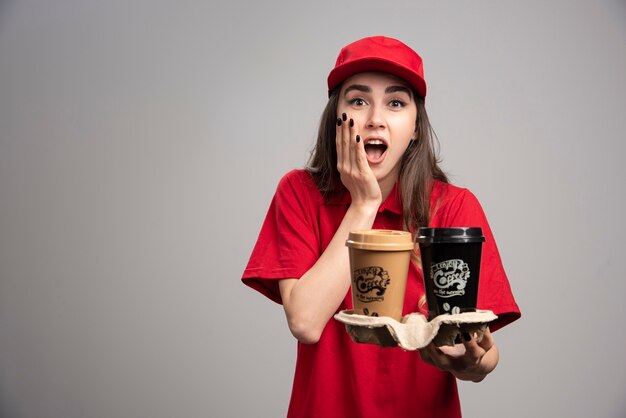 Mooie leveringsvrouw die haar gezicht en koffiekopjes houdt.