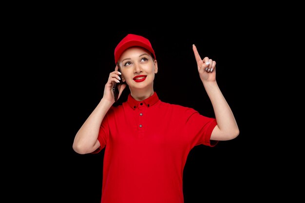 Mooie meid aan de telefoon die omhoog wijst in een rode dop met een shirt en felle lippenstift