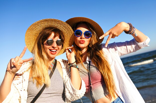 Mooie meisjes die selfie maken en luchtkussen naar de camera sturen, zomerse reistijd, boho-kleding, zonnebrillen en strohoeden.