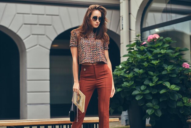 Mooie modieuze brunette die trendy kleding en zonnebril draagt.