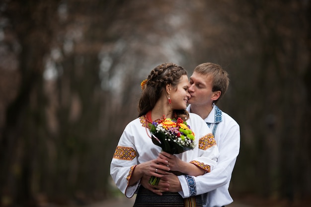 Mooie Oekraïense bruid en bruidegom in native borduurpakken op de achtergrond van bomen in een park, traditionele trouwceremonie