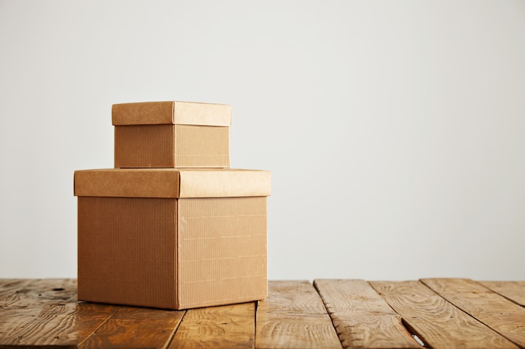 Gratis Foto mooie oude ongelijke houten tafel met twee lege soortgelijke kartonnen dozen met covers tegen witte muur achtergrond