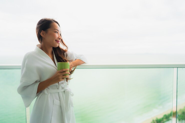 Gratis Foto mooie portret jonge aziatische vrouwen die koffiekop houden bij openluchtbalkon met overzeese oceaanmening