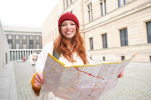 Gratis foto mooie roodharige vrouw toerist met stadsplattegrond verkent bezienswaardigheden historisch oriëntatiepunt rondlopen