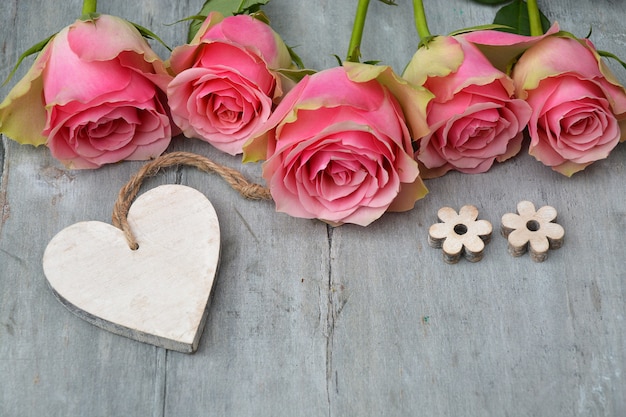 Gratis foto mooie roze rozen met een houten hart en kleine bloemen op een houten ondergrond