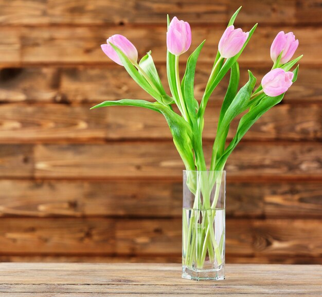 Mooie roze tulpen in vaas op tafel op houten achtergrond