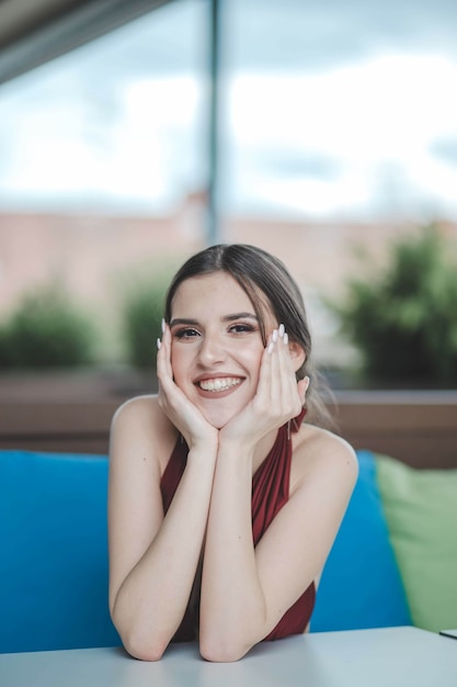 Mooie sexy blanke vrouw in een rode rugloze jurk zittend op een terras