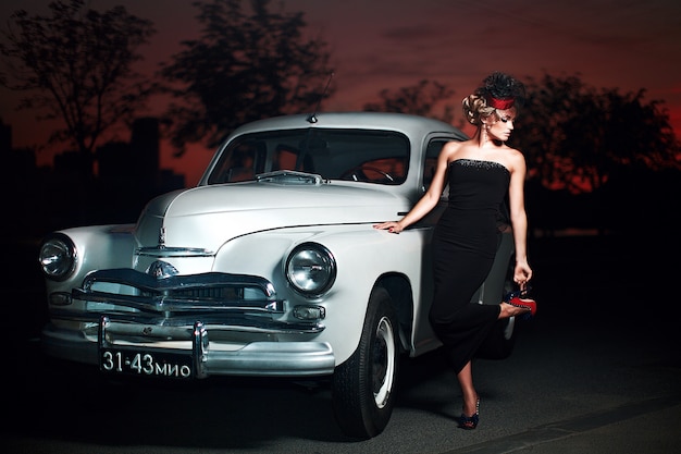 Mooie sexy mode blond meisje model met lichte make-up en krullend kapsel in retro-stijl zitten in oude auto