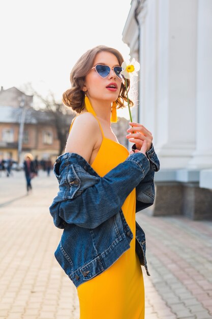 Mooie sexy stijlvolle vrouw in gele stijlvolle jurk dragen spijkerjasje, trendy outfit, lente zomer modetrend, zonnige, blauwe zonnebril, straatmode, hipster stijl, modieuze accessoires