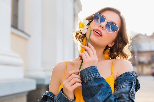 Mooie sexy stijlvolle vrouw in gele stijlvolle jurk dragen spijkerjasje, trendy outfit, lente zomer modetrend, zonnige, blauwe zonnebril, straatmode, hipster stijl, modieuze accessoires