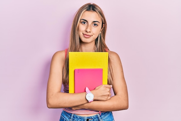 Mooie Spaanse vrouw met boeken denkende houding en nuchtere uitdrukking die zelfverzekerd kijkt