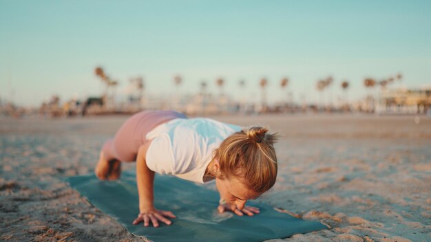 Mooie sportieve vrouw die in openlucht op yogamat uitoefent Geschiktheidsmeisje in sportkleding die yoga op strand beoefent