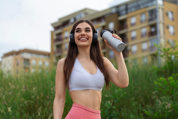 Gratis foto mooie sportieve vrouw drinkwater tijdens het rusten van oefening mooie vrouwelijke atleet permanent buitenshuis drinkwater uit haar fles fitness vrouw een pauze nemen na het uitvoeren van training