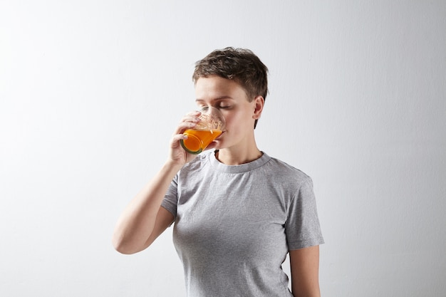 Mooie sportieve vrouw met een gezond perfecte huid in basic grijs t-shirt die droomt haar verse biologische wortels sinaasappelsap drinkt