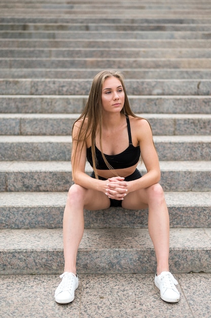 Mooie sportieve vrouw zittend op trappen en wegkijken