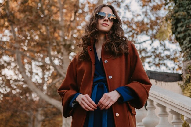 Mooie stijlvolle lachende magere vrouw met krullend haar lopen in straat trappen gekleed in warme bruine jas en blauw pak, herfst trendy mode Streetstyle
