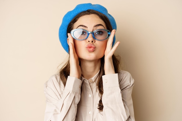 Mooie stijlvolle vrouw in zonnebril die luchtkus blaast op handen in de buurt van lippen die zacht en flirterig staren...