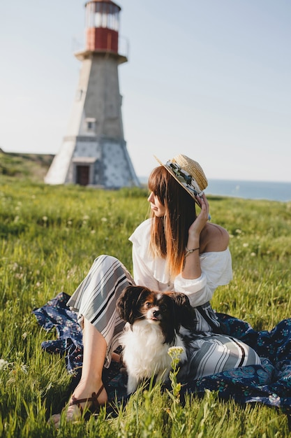 Mooie stijlvolle vrouw op het platteland, met een hond, een gelukkige positieve stemming, zomer, strooien hoed, outfit in bohemienstijl