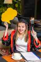 Gratis foto mooie student die een ideebord vasthoudt en haar vinger opsteekt terwijl ze naar de camera glimlacht