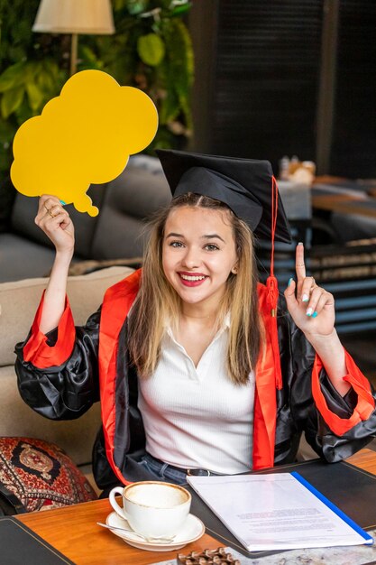 Mooie student die een ideebord vasthoudt en haar vinger opsteekt terwijl ze naar de camera glimlacht