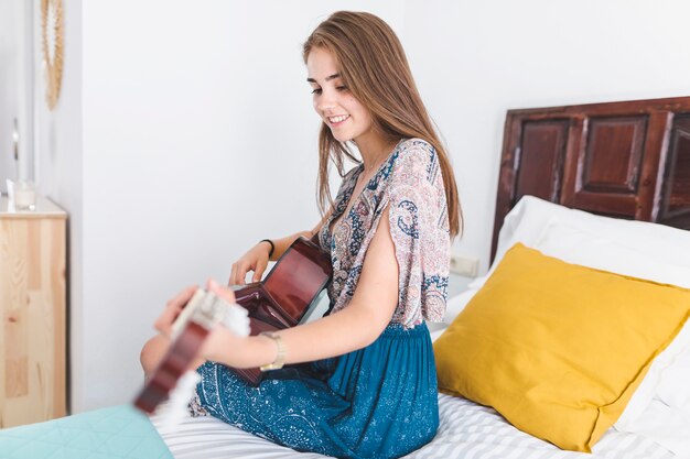 Mooie tiener het spelen gitaar in slaapkamer