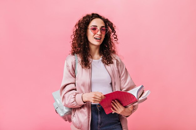 Mooie tiener in roze jasje met notitieboekjes op geïsoleerde achtergrond