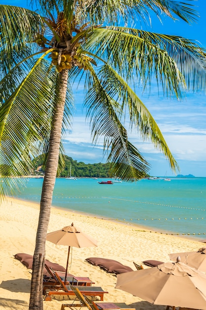 Mooie tropische strandoverzees en oceaan met kokospalm en paraplu en stoel op blauwe hemel