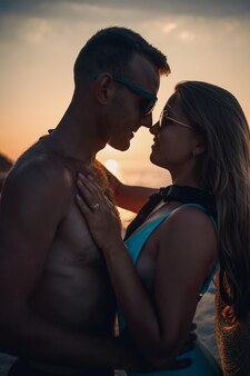 Mooie verliefde paar op de achtergrond van de zonsondergang aan zee jonge vrouw en man knuffelen aan zee bij zonsondergang