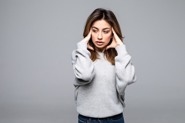 Mooie verstoorde jonge vrouw die sweater status draagt, die aan een hoofdpijn lijdt die over grijze muur wordt geïsoleerd