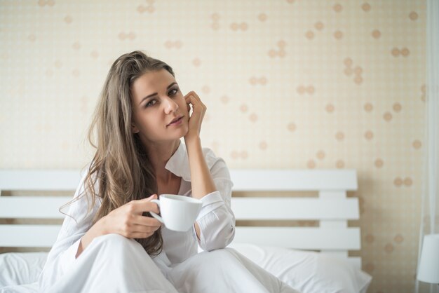 Mooie vrouw bij haar slaapkamer het drinken koffie in de ochtend