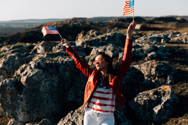 Gratis foto mooie vrouw die amerikaanse vlaggen op rotsachtige achtergrond golft