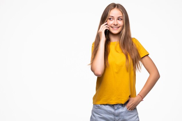 Mooie vrouw die bij celtelefoon spreekt, die over witte muur wordt geïsoleerd