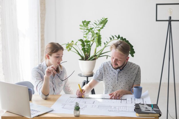 Mooie vrouw die blauwdruk bekijkt terwijl haar collega die aan het werkt