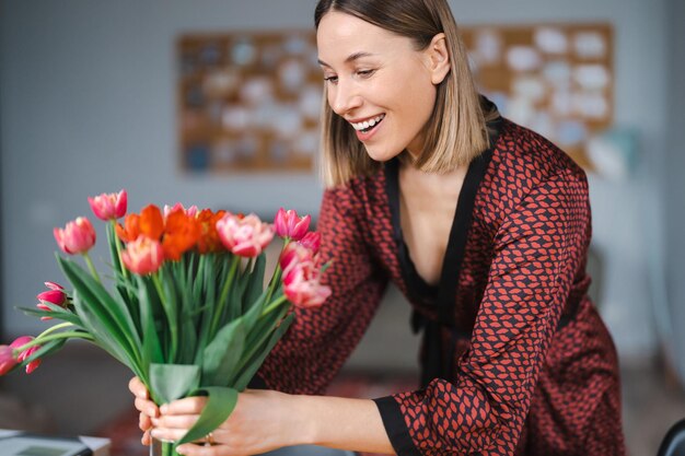 Mooie vrouw die bloemen schikt, gepresenteerd door haar man thuis, gelukkig en vreugdevol