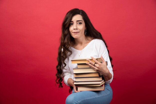 Mooie vrouw die boeken op een rode achtergrond draagt. Hoge kwaliteit foto