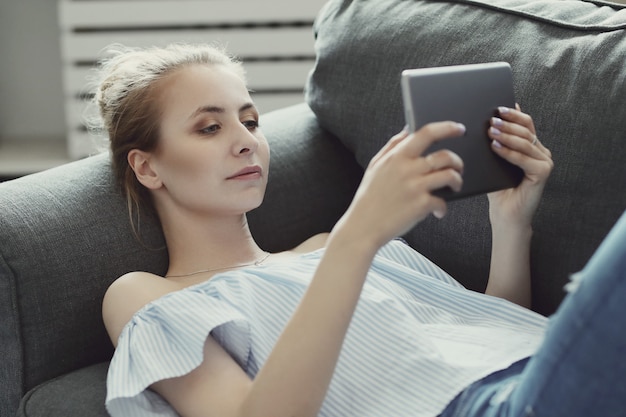 Mooie vrouw die digitale tablet gebruiken, die op bank liggen