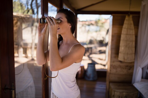 Gratis foto mooie vrouw die door verrekijkers van venster kijkt